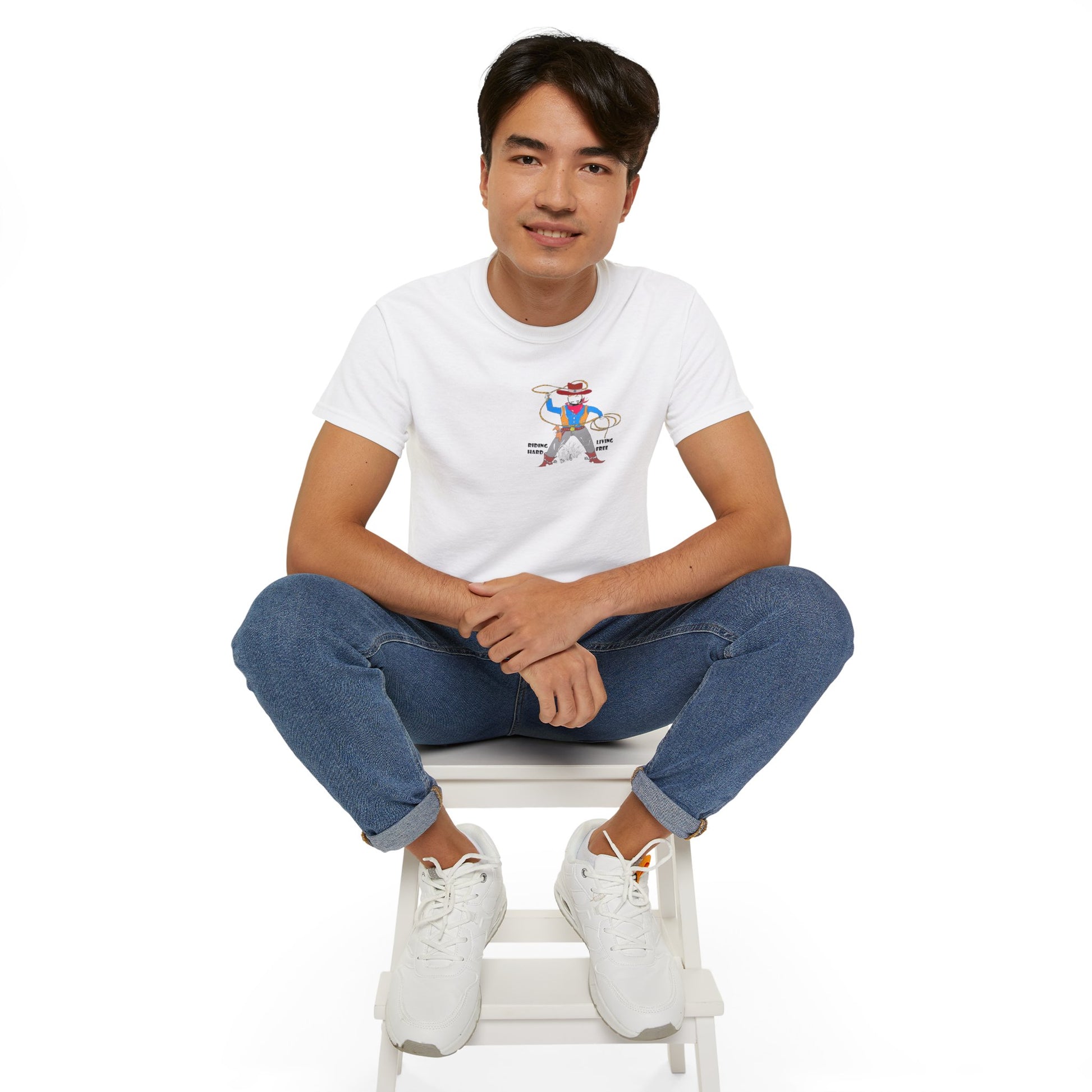 Front view of a man model wearing a white t-shirt with a cowboy graphic design, sitting on a white stool against a white background