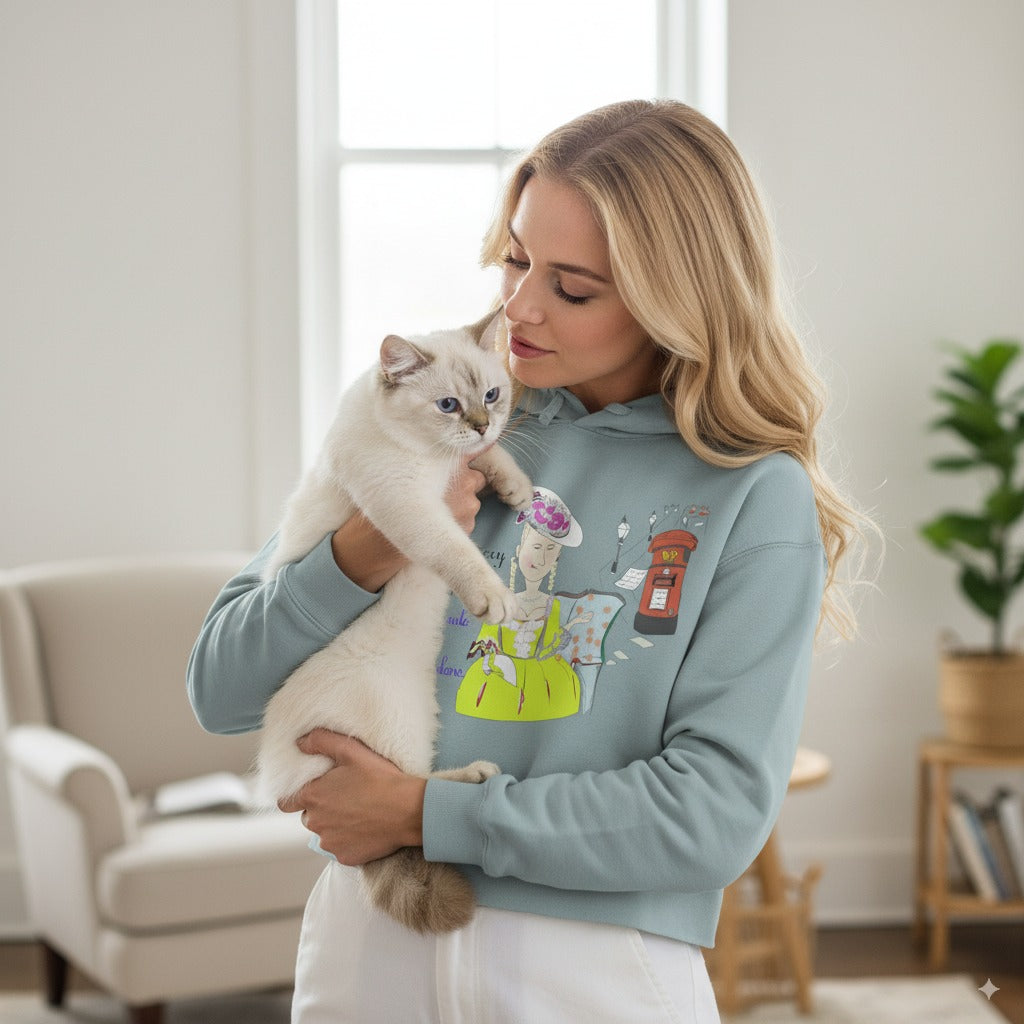 Woman holding a cat wearing a light blue sweatshirt with a colorful vintage dressed English lady graphic and text in a living room.