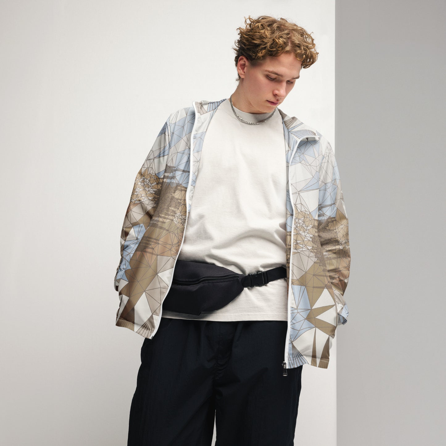 Person wearing an abstract patterned windbreaker over a white sweater with black pants on a plain background