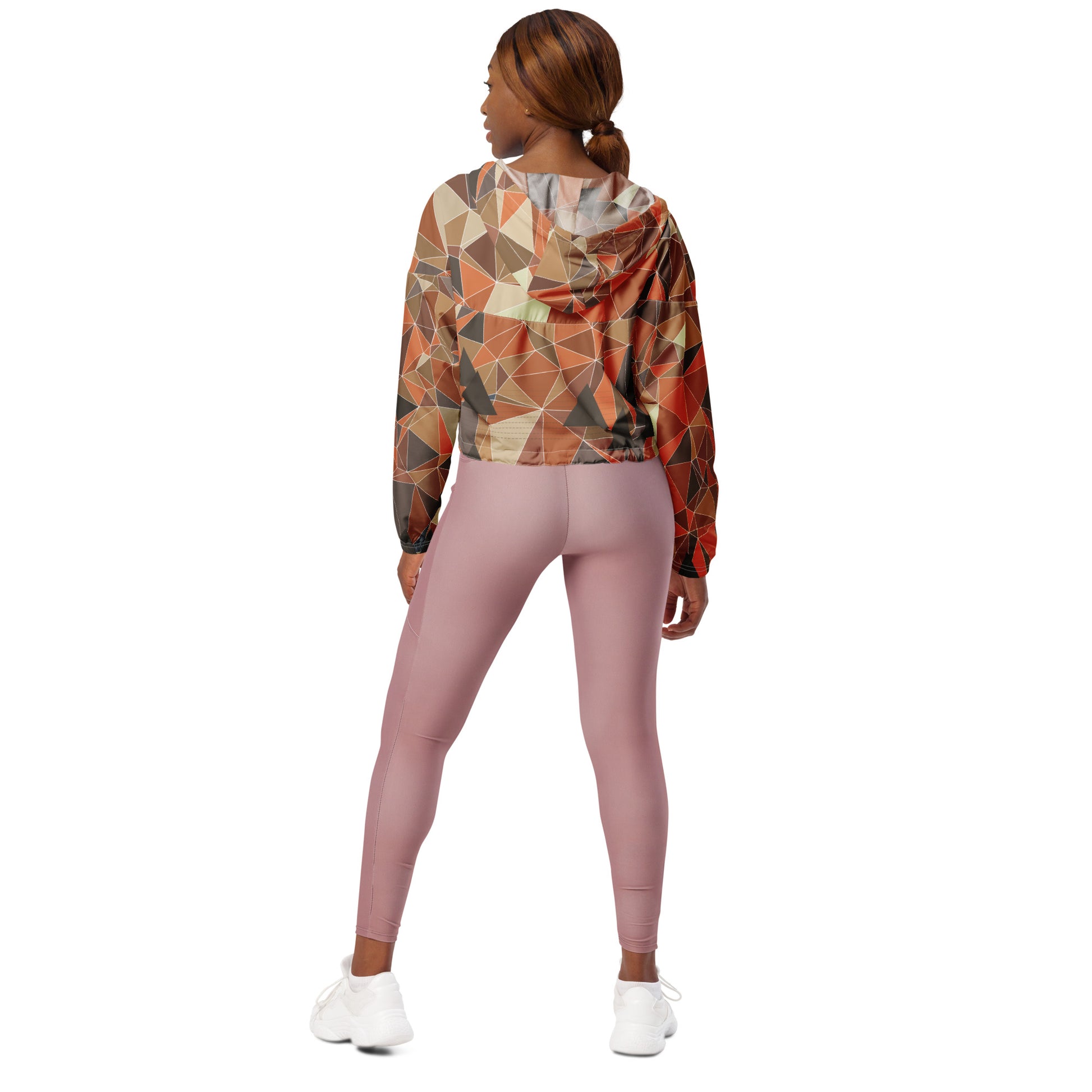 Person wearing a cropped multicolor geometric patterned windbreaker jacket and pink leggings on a white background