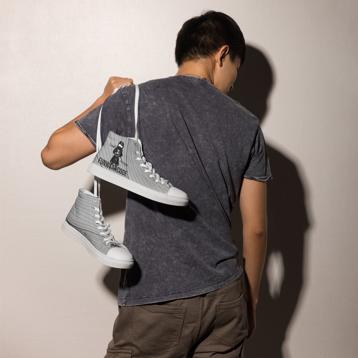 Person holding a pair of gray high-top sneakers with a ninja graphic and 'Fun Wear Code' text logo against a plain background