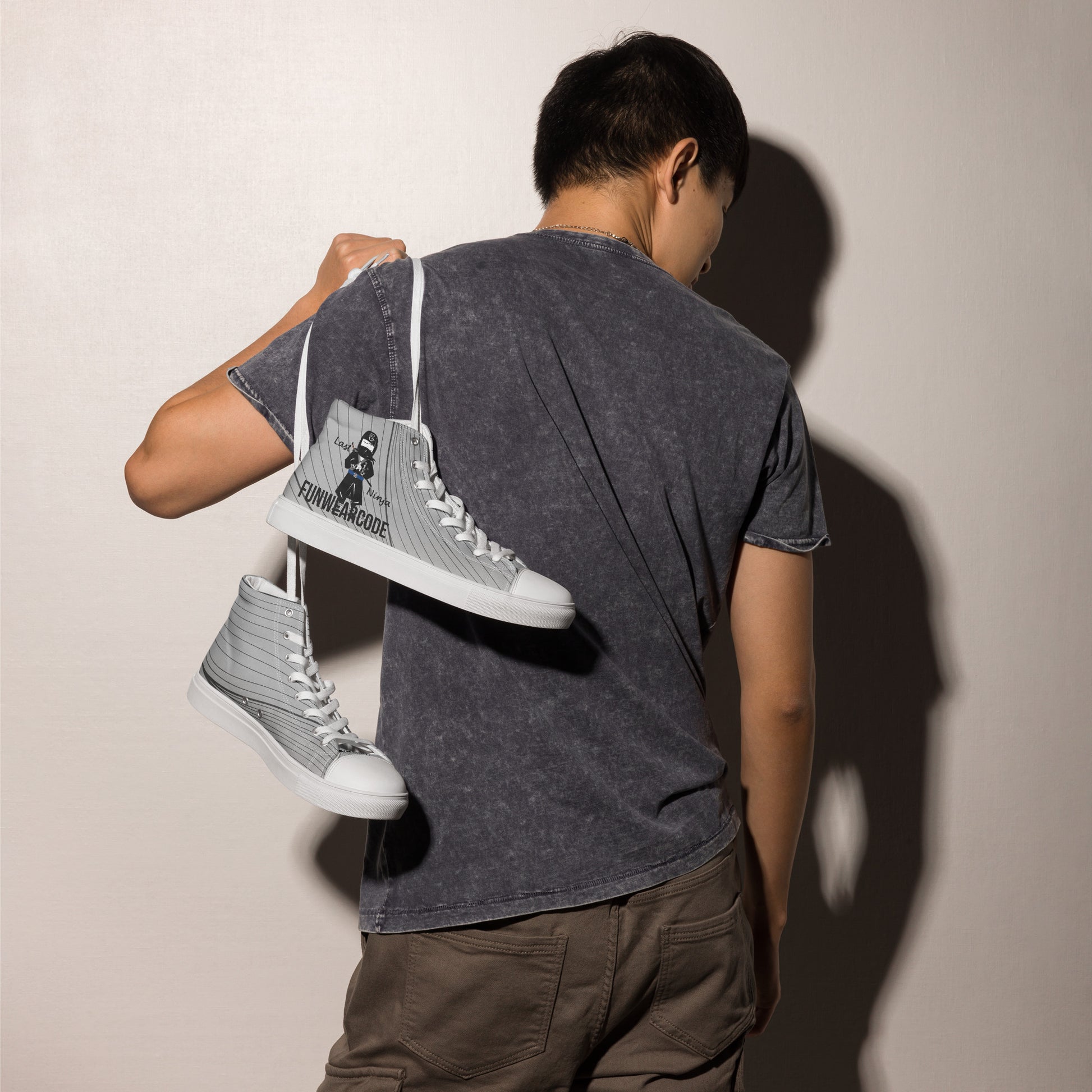 Person holding a pair of gray high-top sneakers with a ninja graphic and 'Fun Wear Code' text logo against a plain background